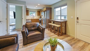 Amplia sala de estar con un sofá de cuero, una mesa de centro con una planta y una zona de cocina con armarios de madera y un refrigerador.