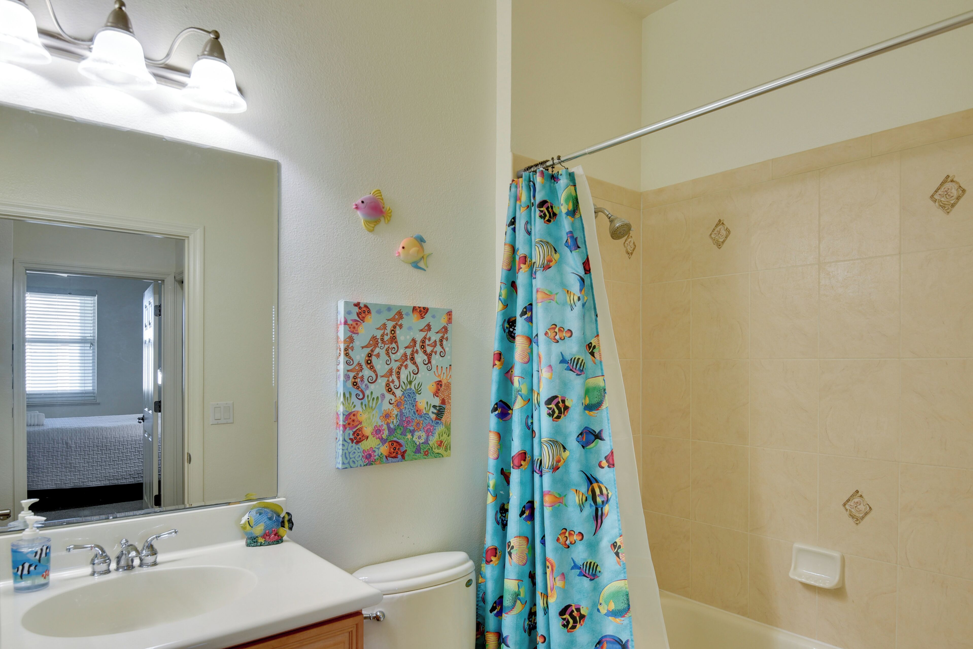 A bathroom with a white sink, a toilet, a shower curtain with fish patterns, a mirror, and a wall-mounted soap dish.