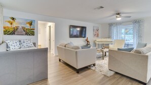 A living room with a sofa, a coffee table, and a TV mounted on the wall. There is a door leading to another room.