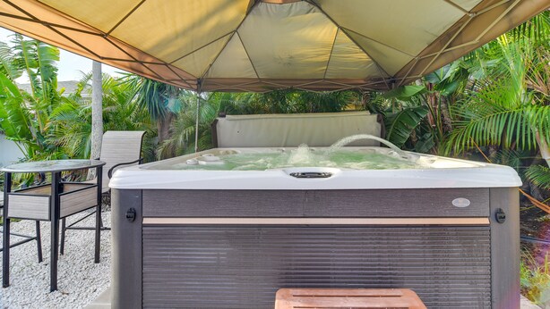 A hot tub under a canopy with a table and chairs nearby.