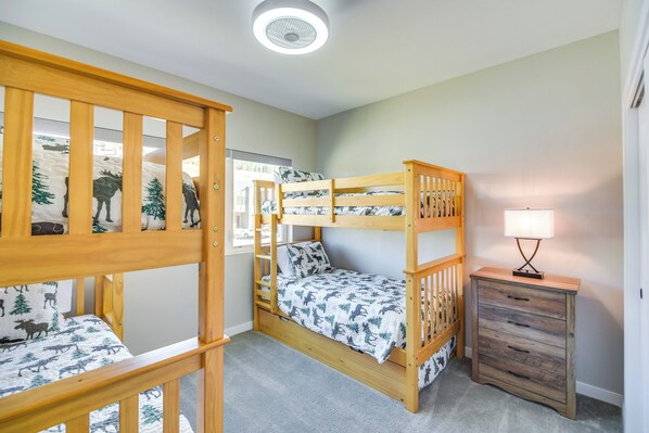 Une chambre avec un lit superposé doté d’une tête de lit en bois, une table de chevet avec une lampe et une fenêtre donnant sur l’extérieur.