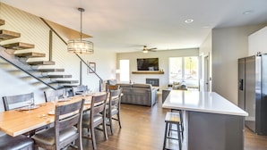 A modern kitchen with a central island, a dining area with wooden chairs and a table, and a staircase with a light fixture. - Ski-in/ski-out Granby Townhouse w/ Private Hot Tub (Granby)