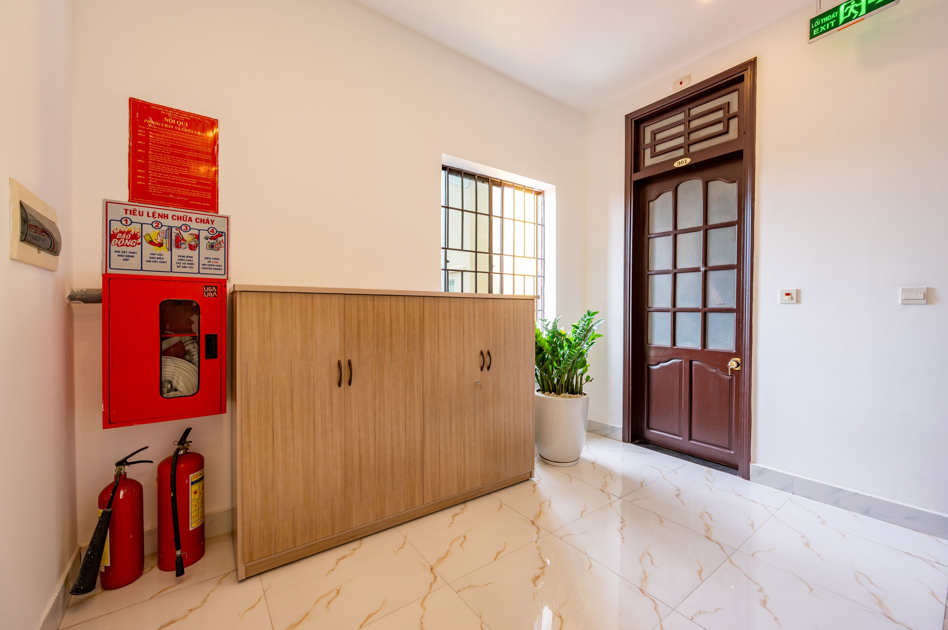 A hotel reception area with a wooden cabinet, a fire extinguisher, a potted plant, and a door with a traditional design.