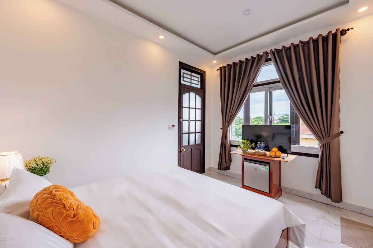 Ein Hotelzimmer mit Bett, Schreibtisch inklusive Computer, Fenster mit Vorhängen und einer Tür mit traditioneller Gestaltung.