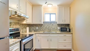 A kitchen with white cabinets, granite countertops, a stainless steel range hood, a microwave, and an oven.