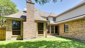A two-story brick house with a chimney, large windows, and a covered patio area.