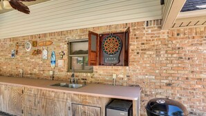 A kitchen with a brick wall, wooden cabinets, a built-in microwave, and a grill.