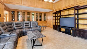 A spacious living room with a large sectional sofa, a flat-screen TV, and wooden paneling. - Expansive Home w/ Pool Table ~ 15 Mi to Galveston! (Texas City)