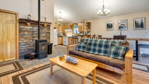 A cozy living room with a stone fireplace, wooden furniture, and a kitchen in the background.