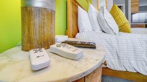 A bed with white and yellow pillows, a remote control, and a lamp on a marble bedside table.