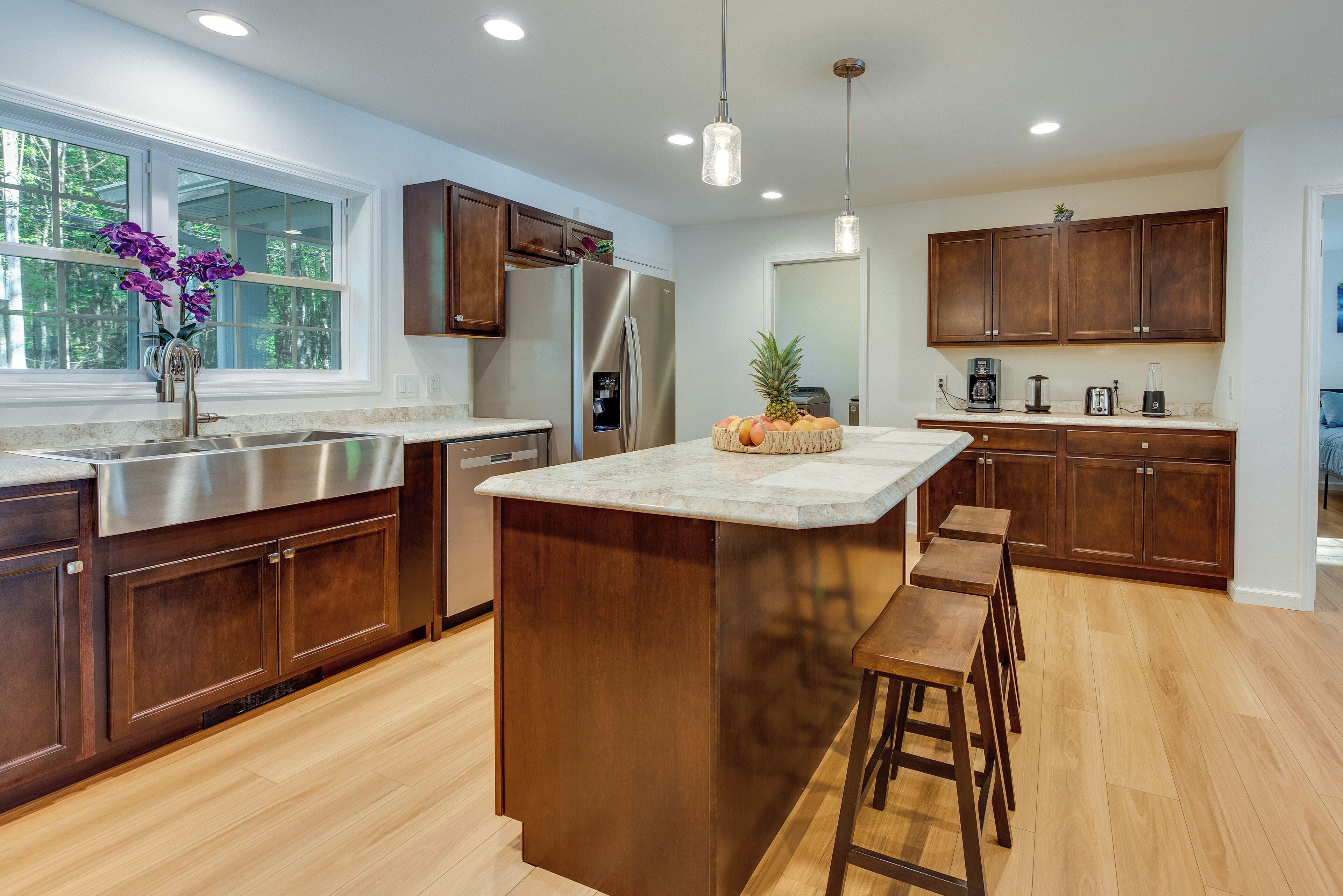Una cocina moderna con armarios de madera, electrodomésticos de acero inoxidable, una isla de mármol y un ventanal grande.
