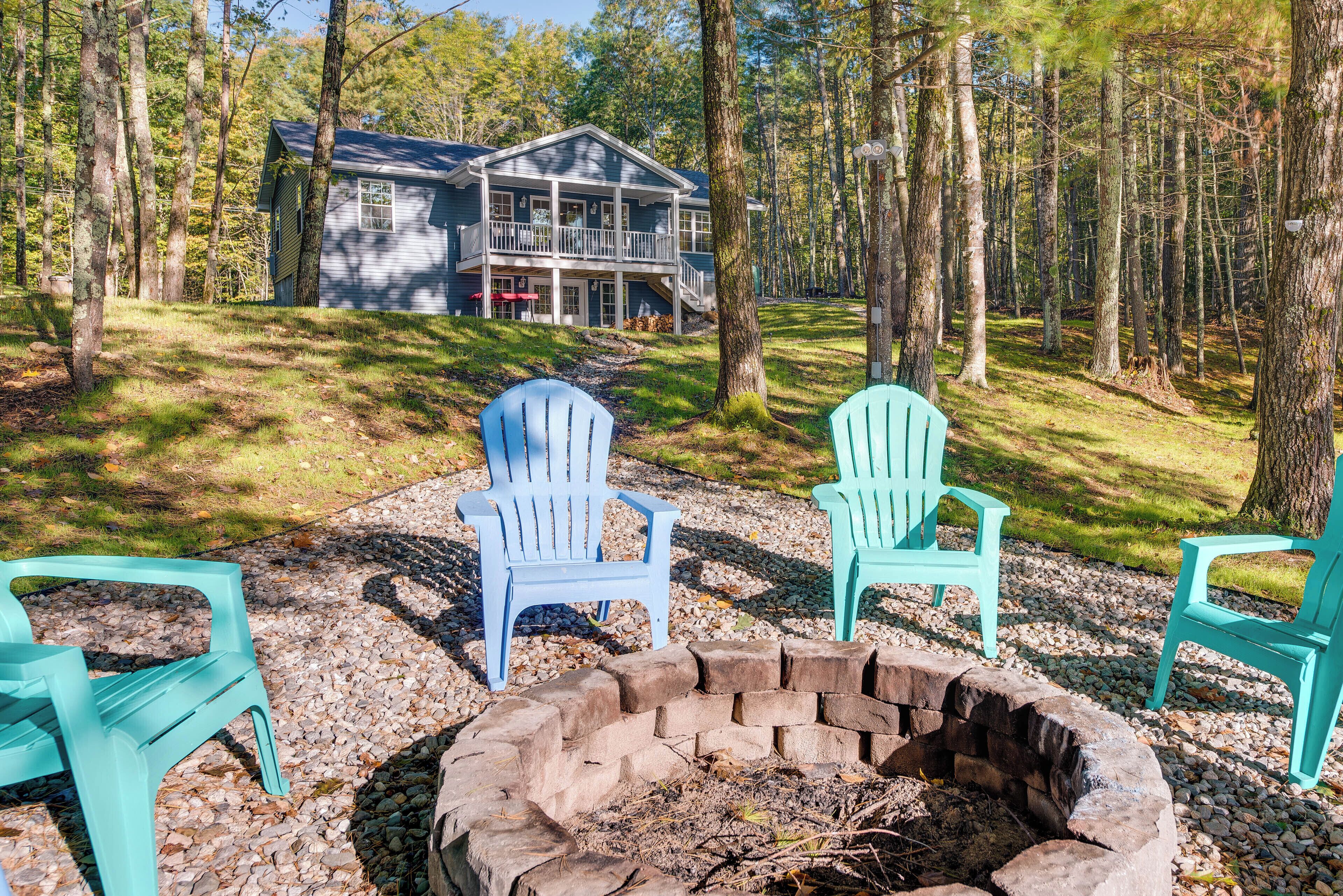 A cabin with a stone fire pit and turquoise Adirondack chairs in a forest setting.