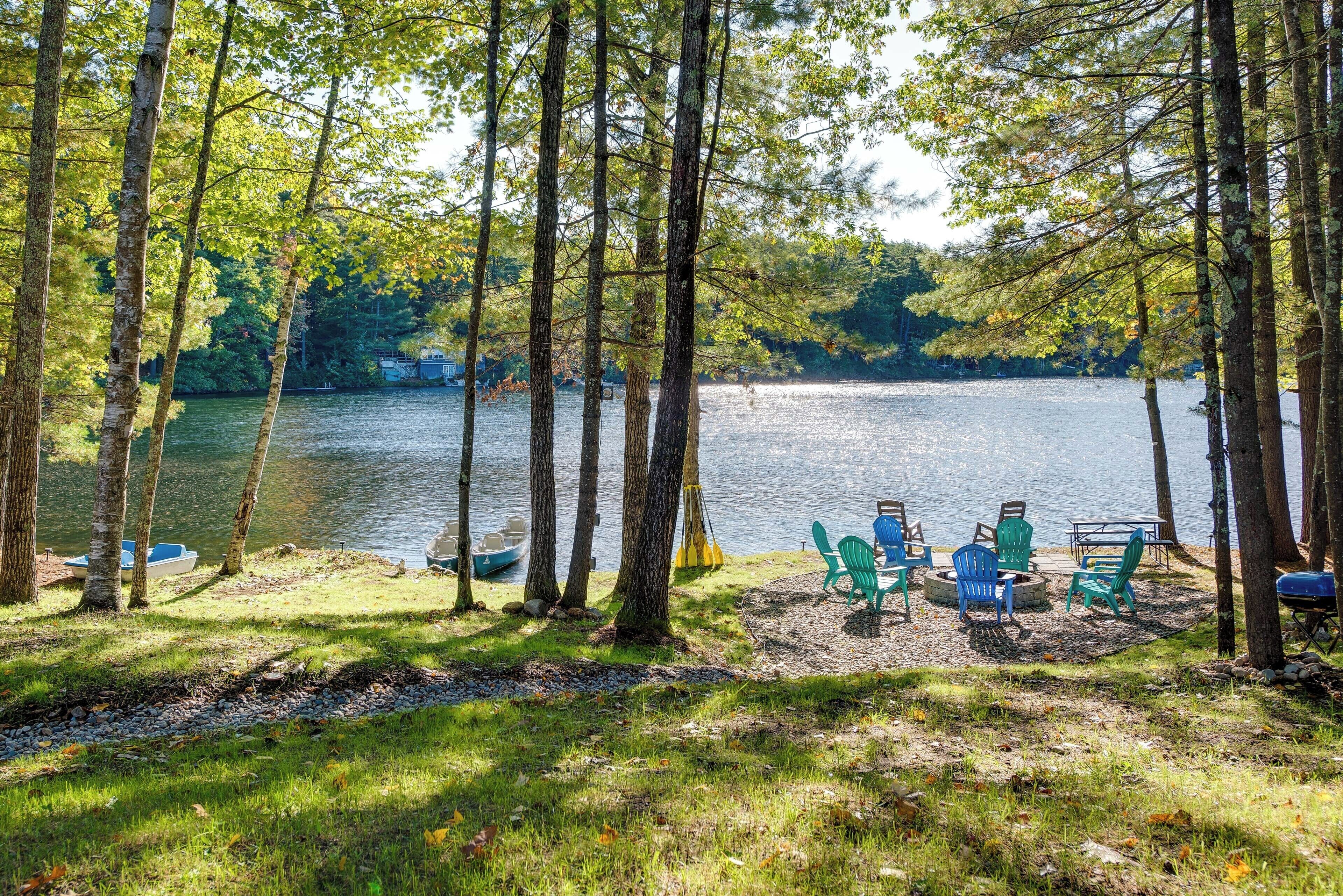 A lakeside campsite with green chairs and a fire pit.