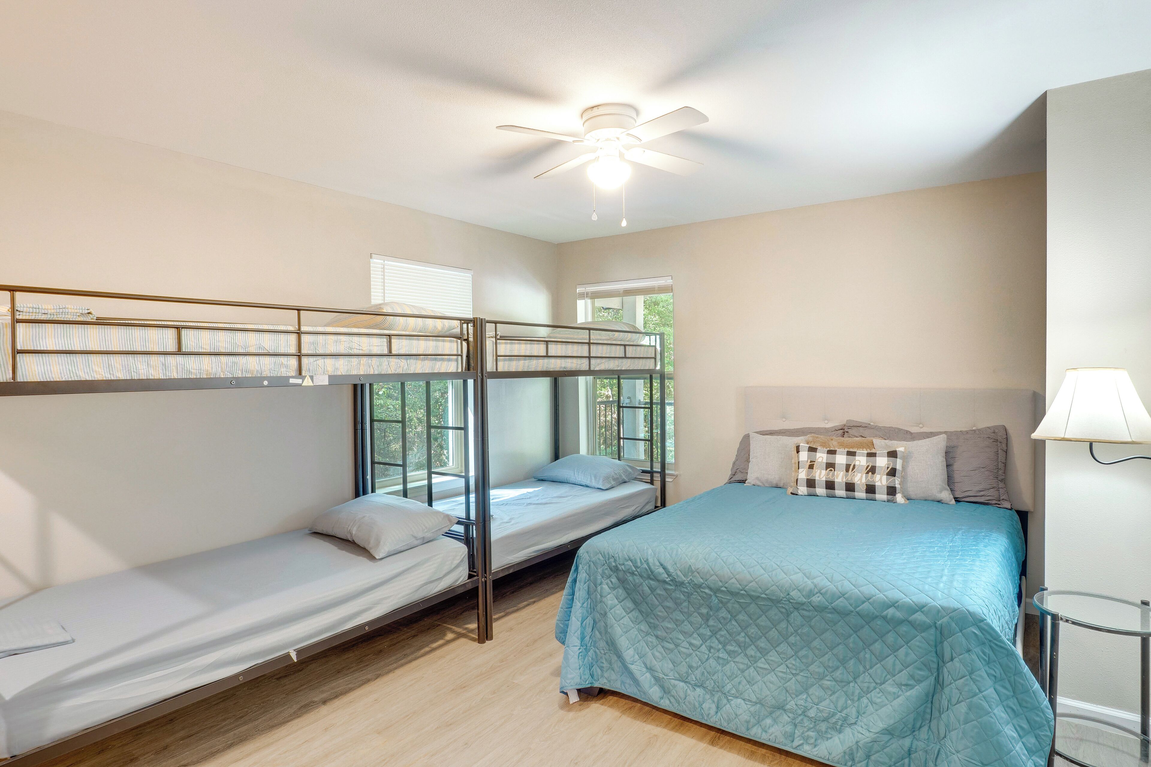 Une chambre avec des lits superposés, un lit simple, un ventilateur de plafond et une fenêtre avec des stores.