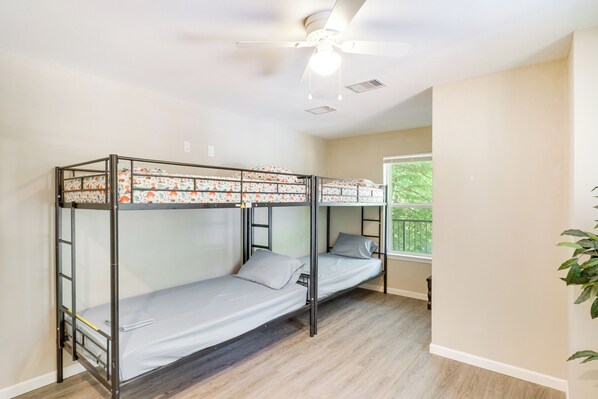 A bunk bed room with a ceiling fan, a window with a view of greenery, and a plant on the right.