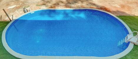 A small, oval-shaped swimming pool with a light-colored edge, surrounded by a green artificial lawn.