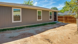 A single-story house with a brown exterior, a front door, and a small front yard with a wooden fence and a tree. - Game Room + Walk to Beach: Gun Barrel City Gem! (Mabank)