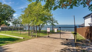 A gated parking area with a clear view of a body of water and a building in the background. - Game Room + Walk to Beach: Gun Barrel City Gem! (Mabank)