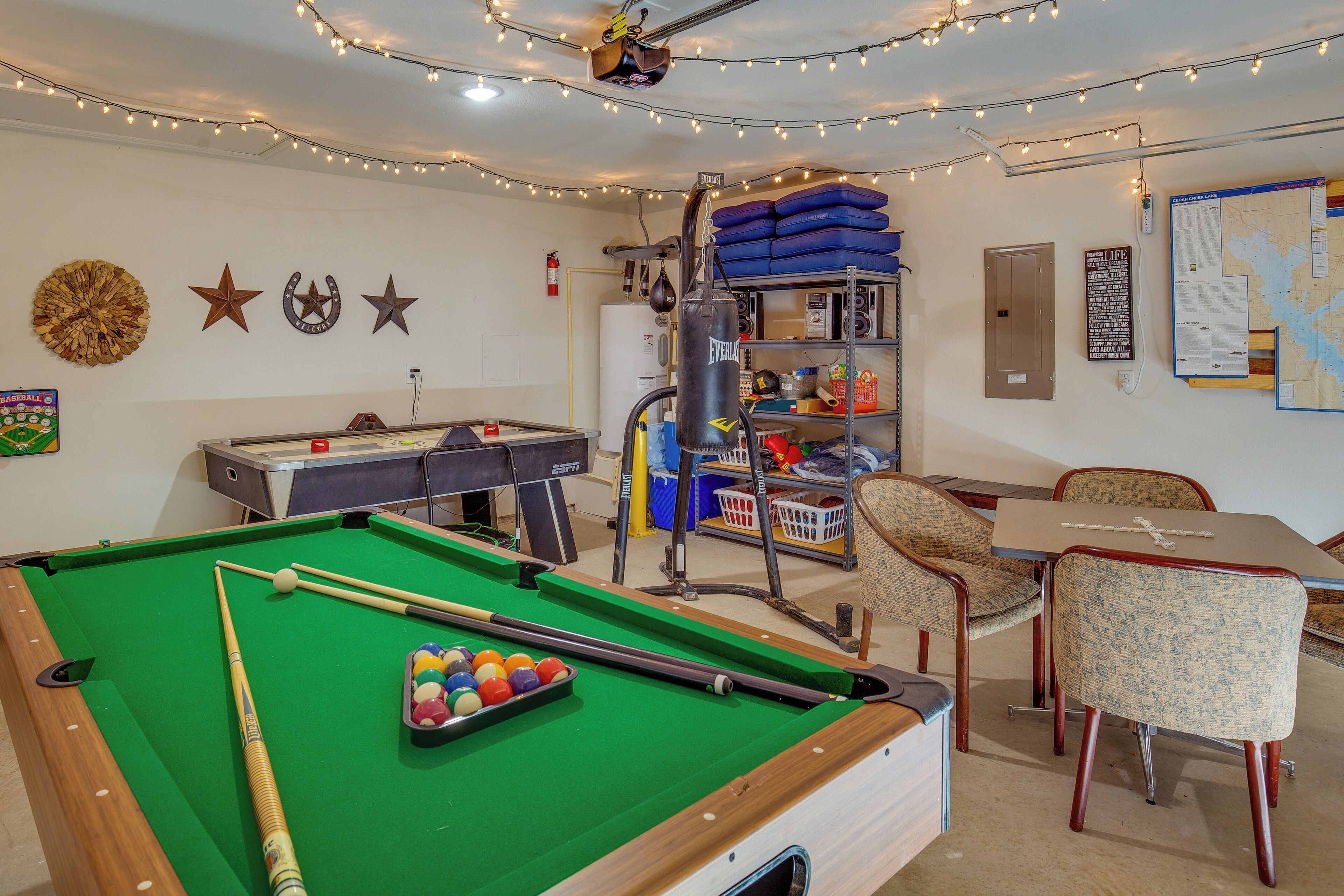 A pool table with balls, a billiard cue, and a pool table cloth. There are chairs and a table with papers.