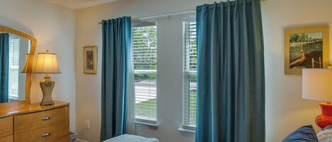 A bedroom with a bed, a dresser, a mirror, and a window with curtains.