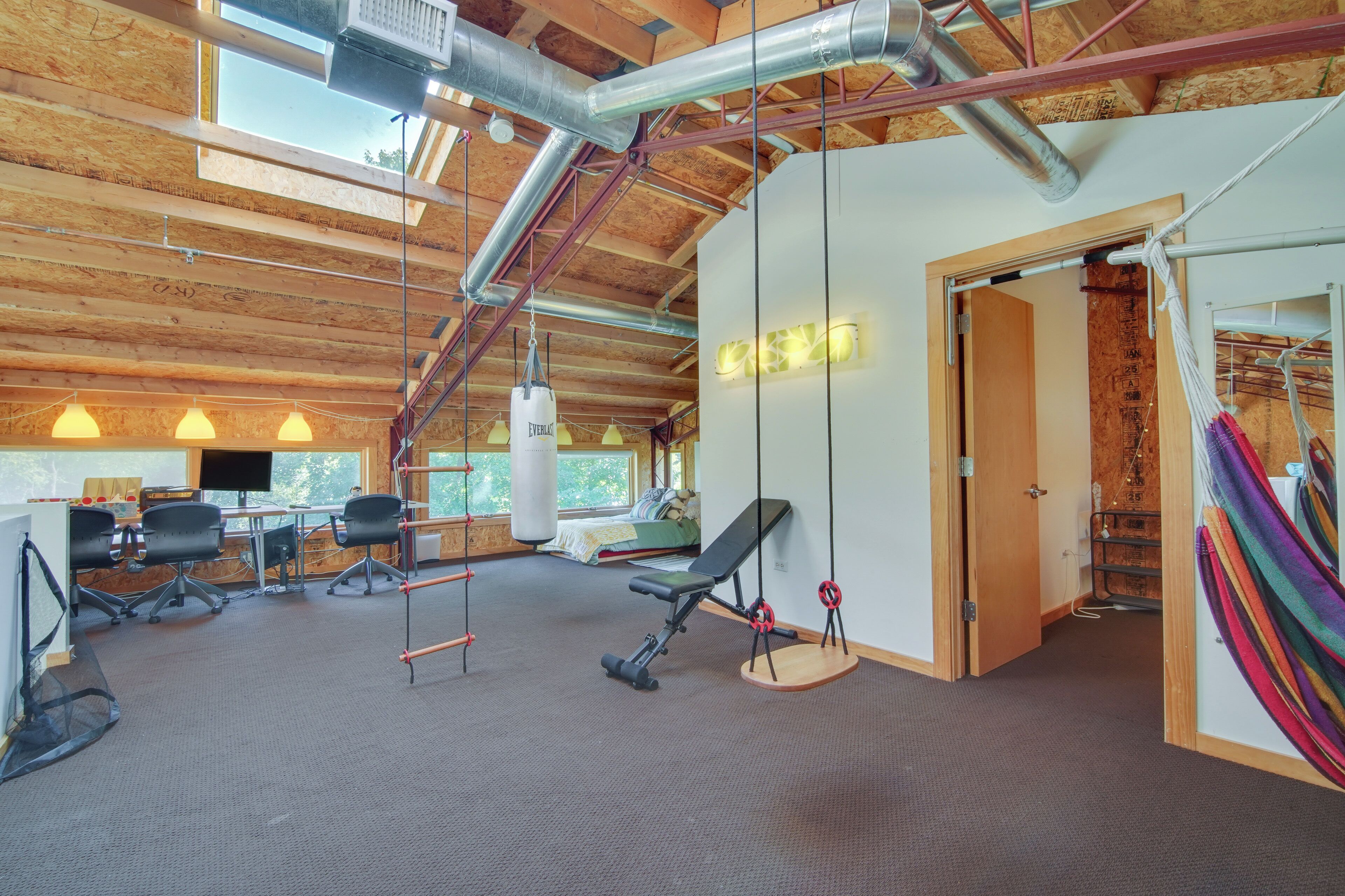 A gym with exercise equipment, a hammock, and a wooden ceiling with visible beams.