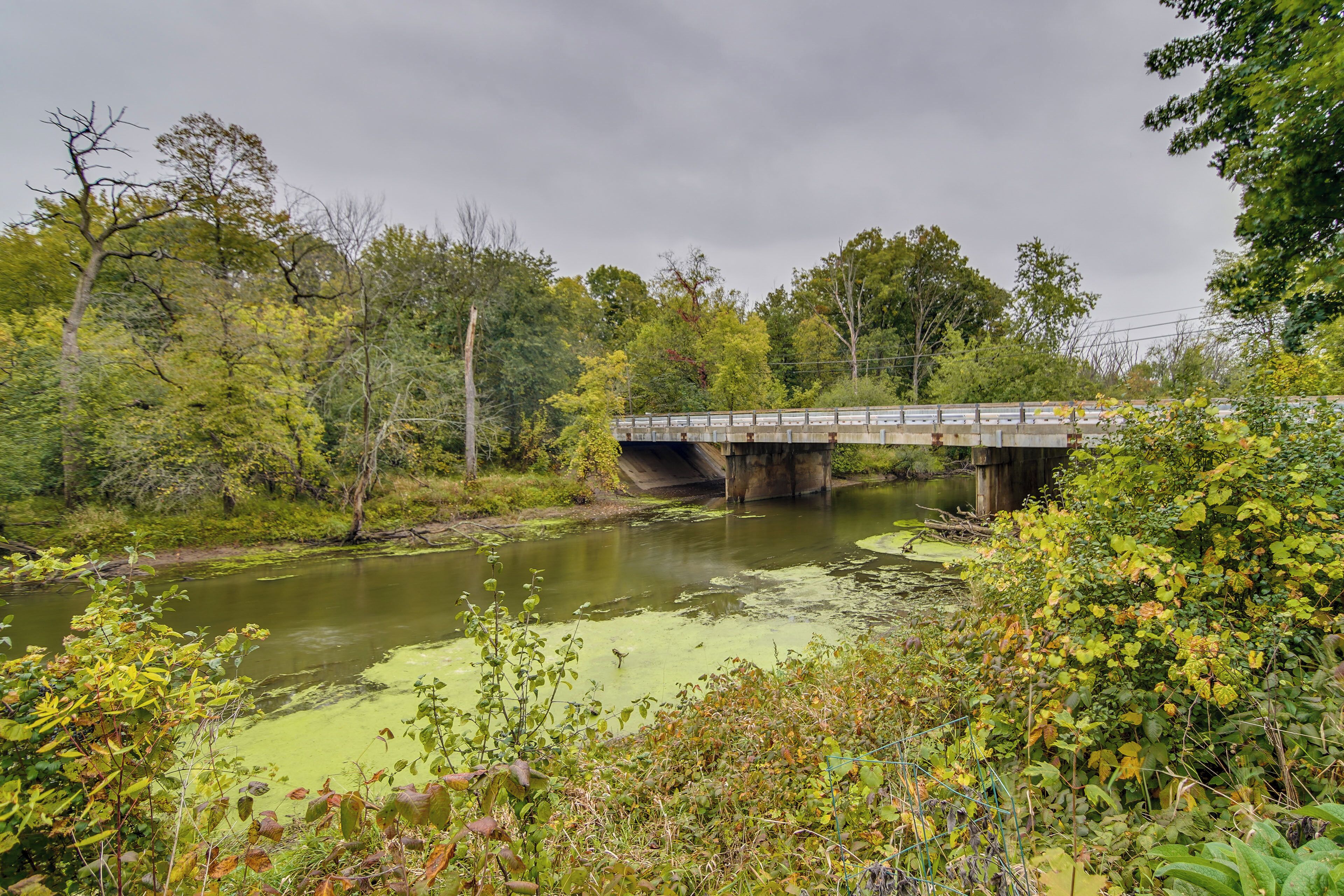 Een brug over een rivier, omringd door groen en met een bewolkte lucht.
