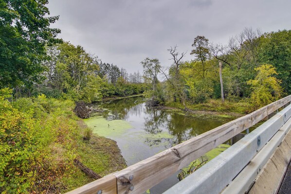 A river with a wooden bridge railing, surrounded by dense greenery and trees.