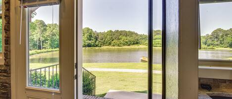A view through a glass door of a lake, a grassy area, and a stone wall.