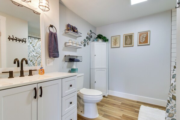 A bathroom with a white toilet, a sink with a mirror, a towel rack, and a cabinet.