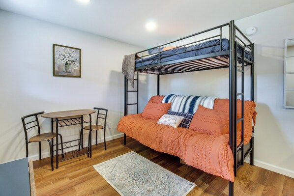 Una cama individual superpuesta con una mesa, sillas, una alfombra y un cuadro en la pared.