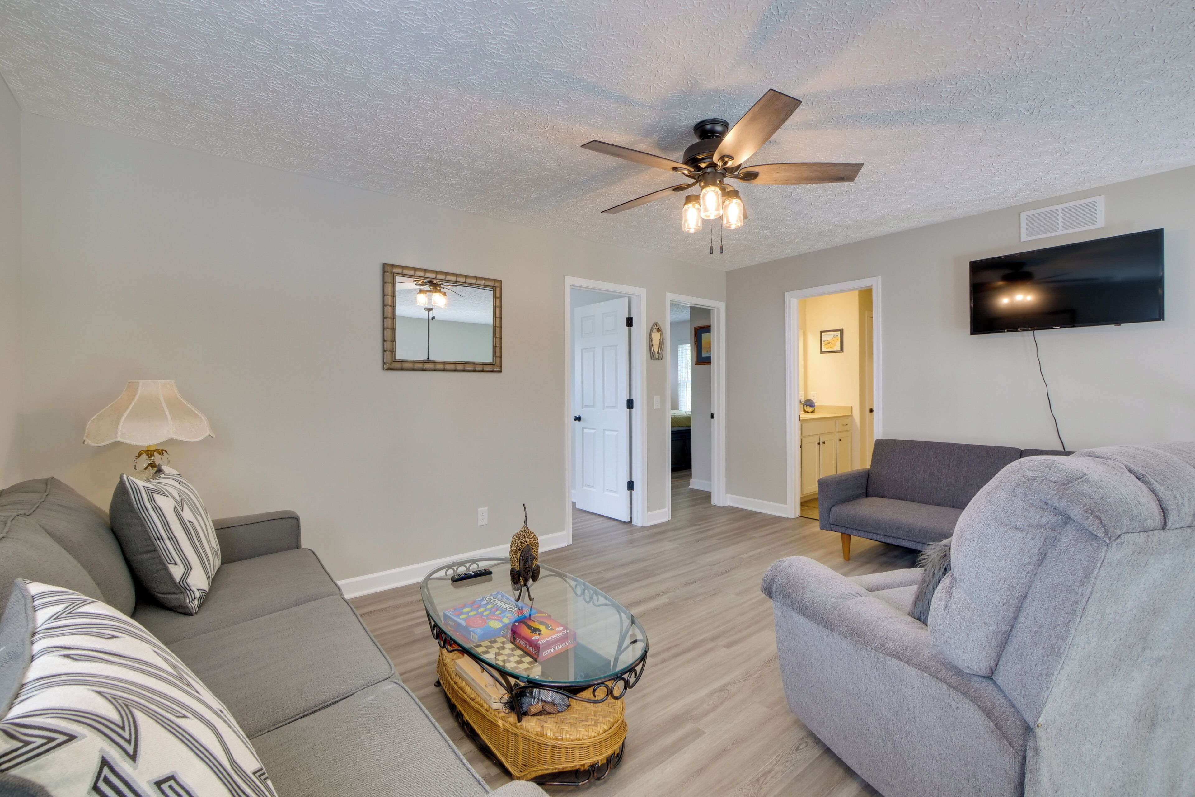 A living room with a ceiling fan, a flat-screen TV, a sofa, a coffee table, and a wicker side table.