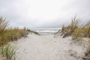 A sandy beach path leading to the ocean, surrounded by grass.