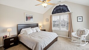 A bedroom with a bed, a nightstand, a chair, a ceiling fan, and a window with curtains.