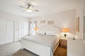 A bedroom with a white bed, two bedside lamps, a ceiling fan, and a nightstand.