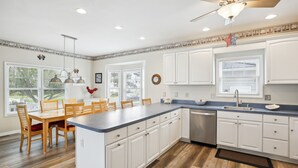 A kitchen with white cabinets, a wooden dining table, and a ceiling fan.