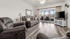 A spacious living room with a large sectional sofa, a flat-screen TV on a white entertainment unit, and a ceiling fan.
