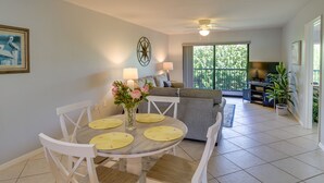 A dining area with a round table, white chairs, and yellow placemats. There is a gray sofa and a ceiling fan in the background. - Florida Retreat w/ Pool, Hot Tub & Beach Access! (Cocoa Beach)