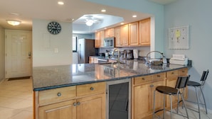 A kitchen with wooden cabinets, a granite countertop, a dishwasher, and a bar stool. - Florida Retreat w/ Pool, Hot Tub & Beach Access! (Cocoa Beach)