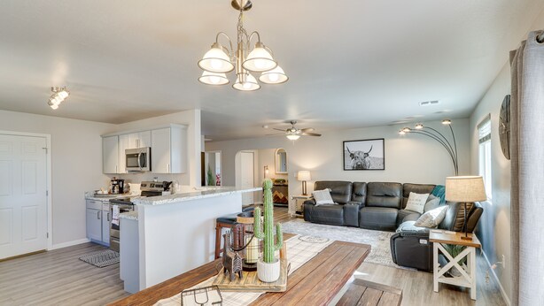 A spacious living area with a wooden dining table, a kitchen with white cabinets, and a modern ceiling fan. - Gold Canyon Vacation w/ Private Patio & Fire Pit! (Gold Canyon)