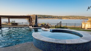 Ein Pool mit Whirlpool, ein überdachter Grillbereich und Blick auf einen See.