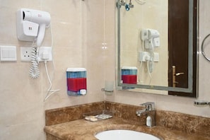 A bathroom with a sink, mirror, hairdryer, and towel dispenser. - SALSBIL AL ALMASI HOTEL (Madinah)