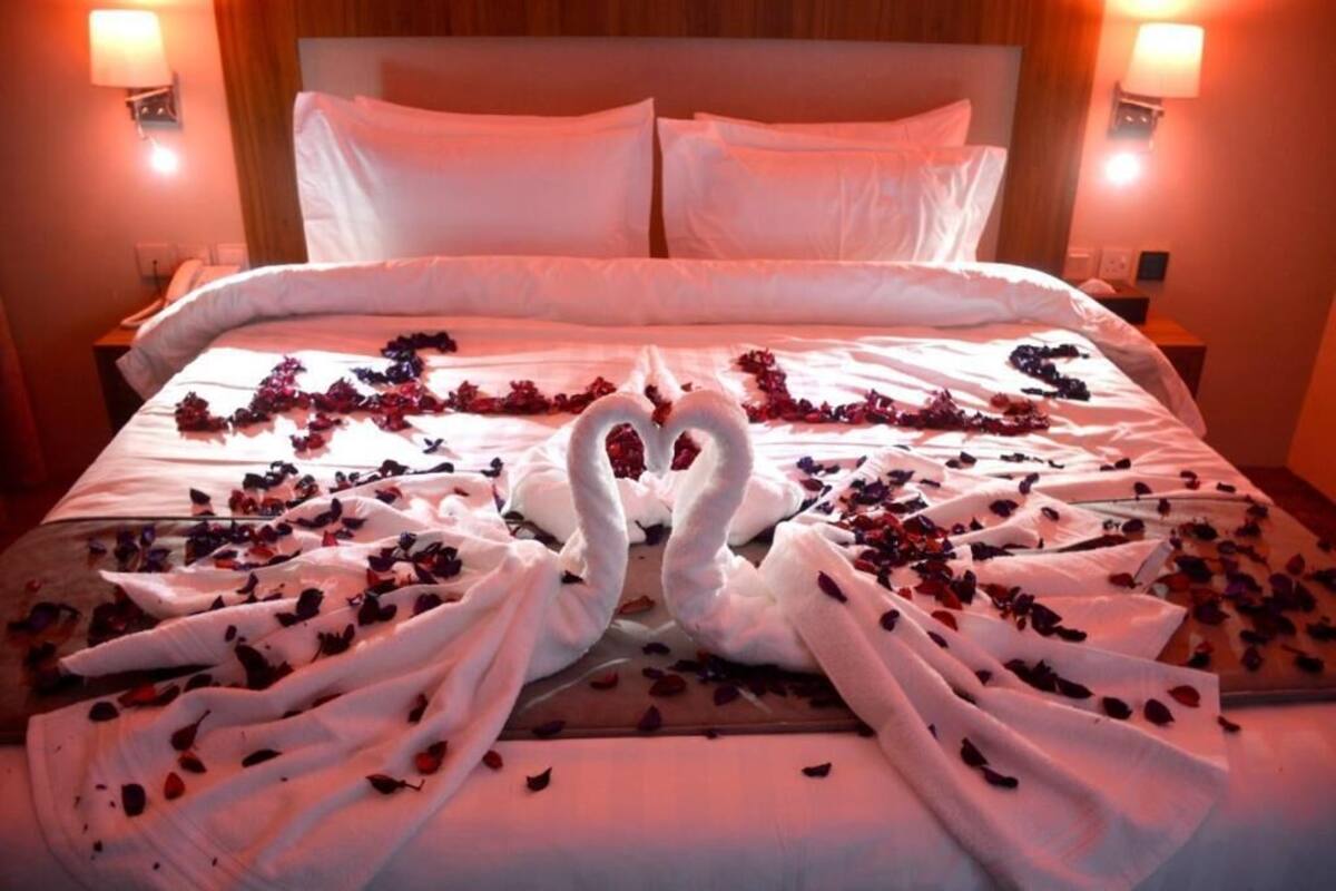 A bed with white linens, two swan-shaped towels, and scattered rose petals.
