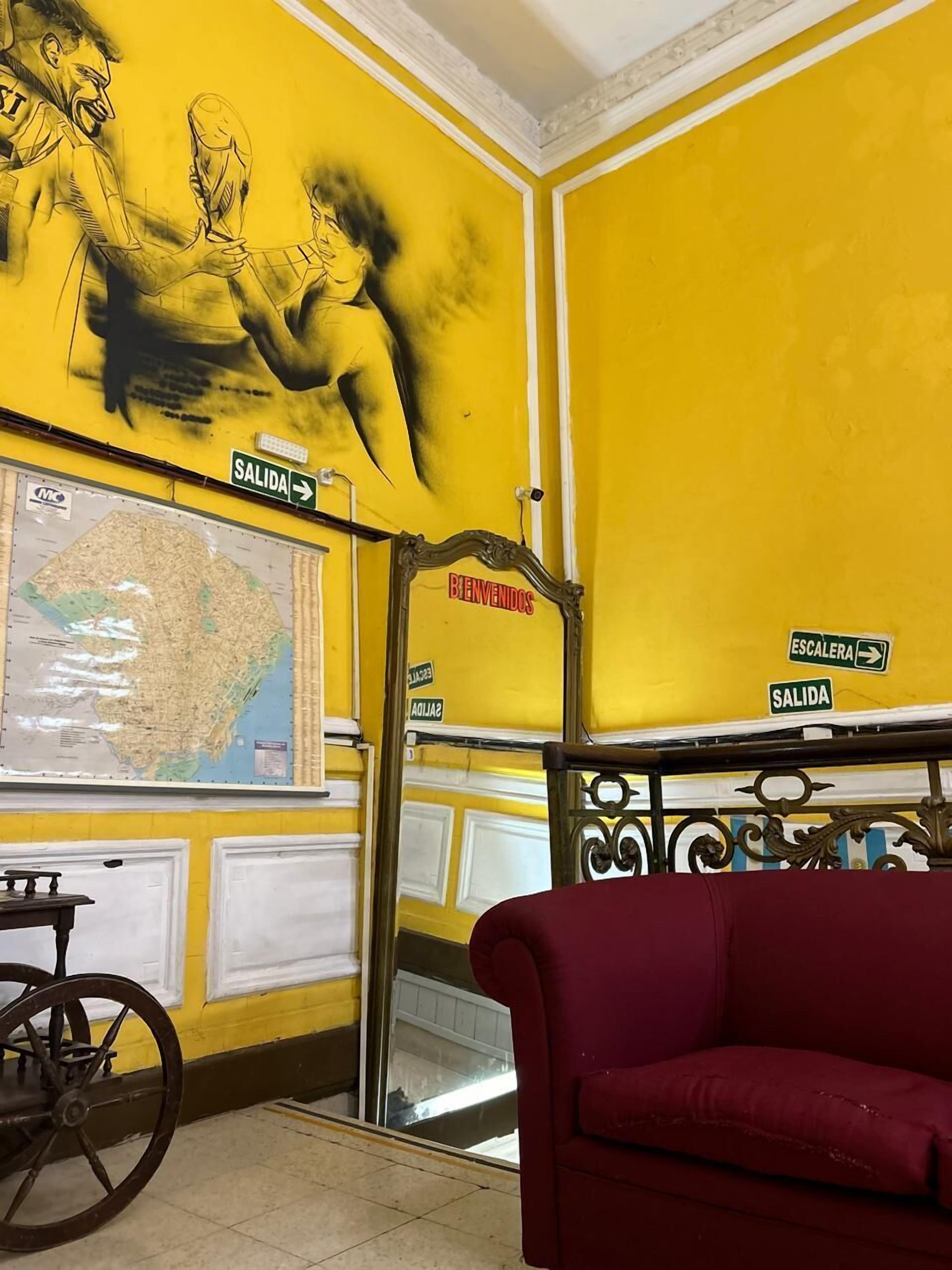 A room with yellow walls, a map on the wall, a red sofa, and a metal railing.