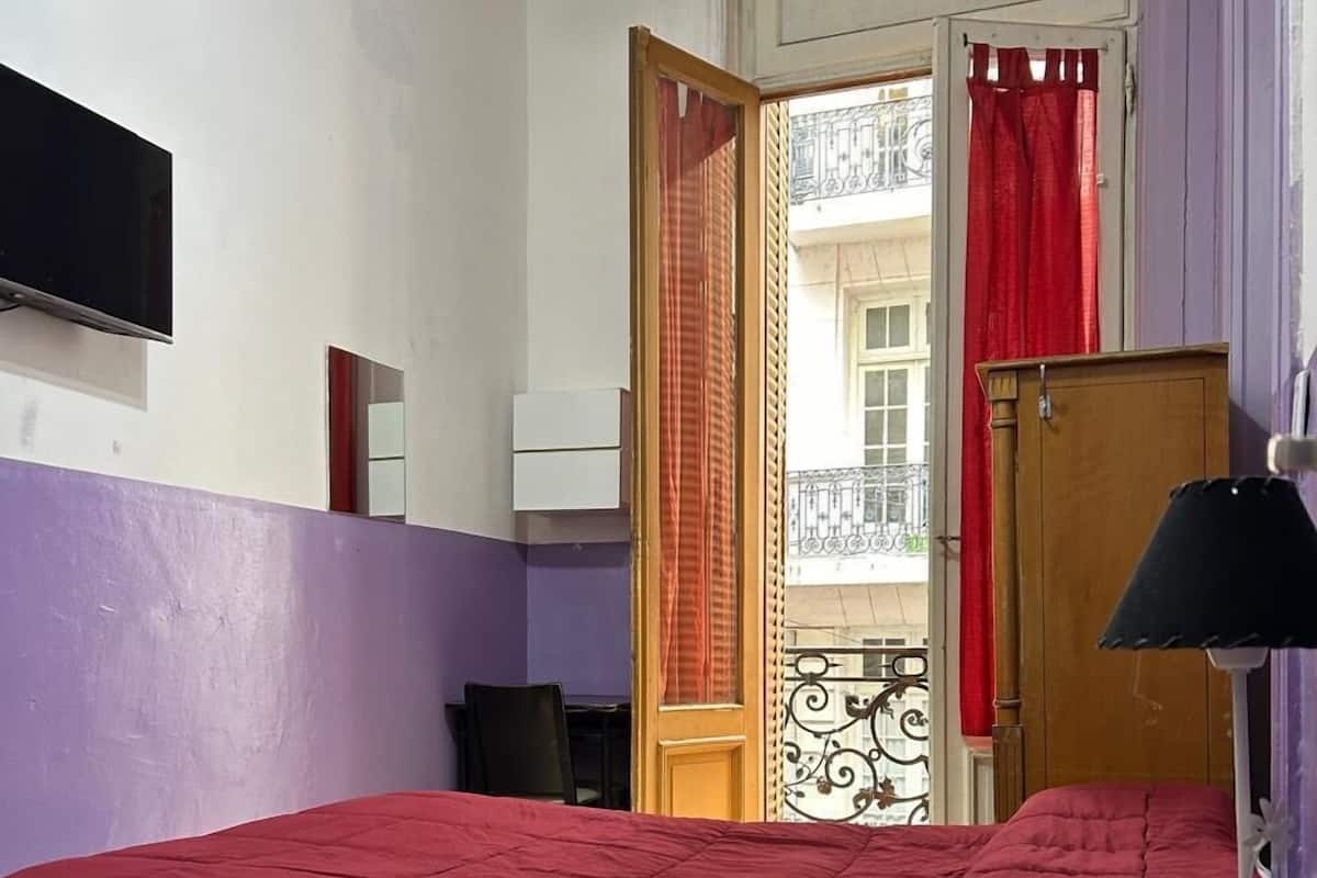 A bedroom with a bed, a nightstand, a lamp, a wardrobe, and a TV mounted on the wall.