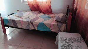 A single bed with a patterned bedspread, a bedside table with a lace tablecloth, and a window with sheer curtains. - Relax and Unwind at our Stunning Vacation Rental in Pointe aux Biches, Mauritius (Pointe Aux Piments)