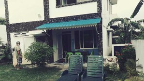 A two-story house with a covered patio area, a small table with chairs, and a lawn with two lounge chairs. - Relax and Unwind at our Stunning Vacation Rental in Pointe aux Biches, Mauritius (Pointe Aux Piments)
