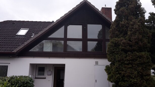 Une maison avec un toit à pignon, de grandes fenêtres et une porte.
