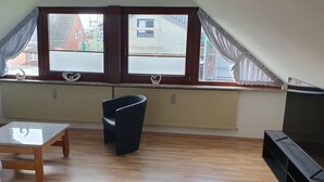 Une pièce avec un plafond en pente, un plancher en bois, une chaise noire, une petite table et un téléviseur.