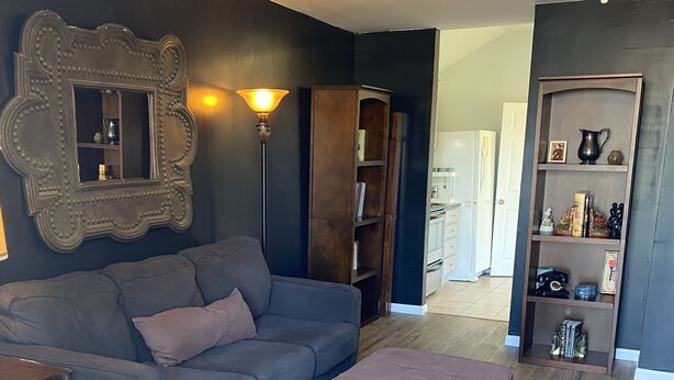 A living room with a dark blue sofa, a wooden floor, a ceiling fan, and a bookshelf. - South Lake Charles Guest Cottage - Country Setting, Rustic Ambience (Lake Charles)