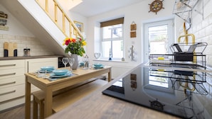 A modern kitchen with a wooden dining table set for two, a staircase with a railing, and a window with a view of the outside. - Morecambe Bay Cottage- Hot Tub/ Jacuzzi/sauna (Morecambe)